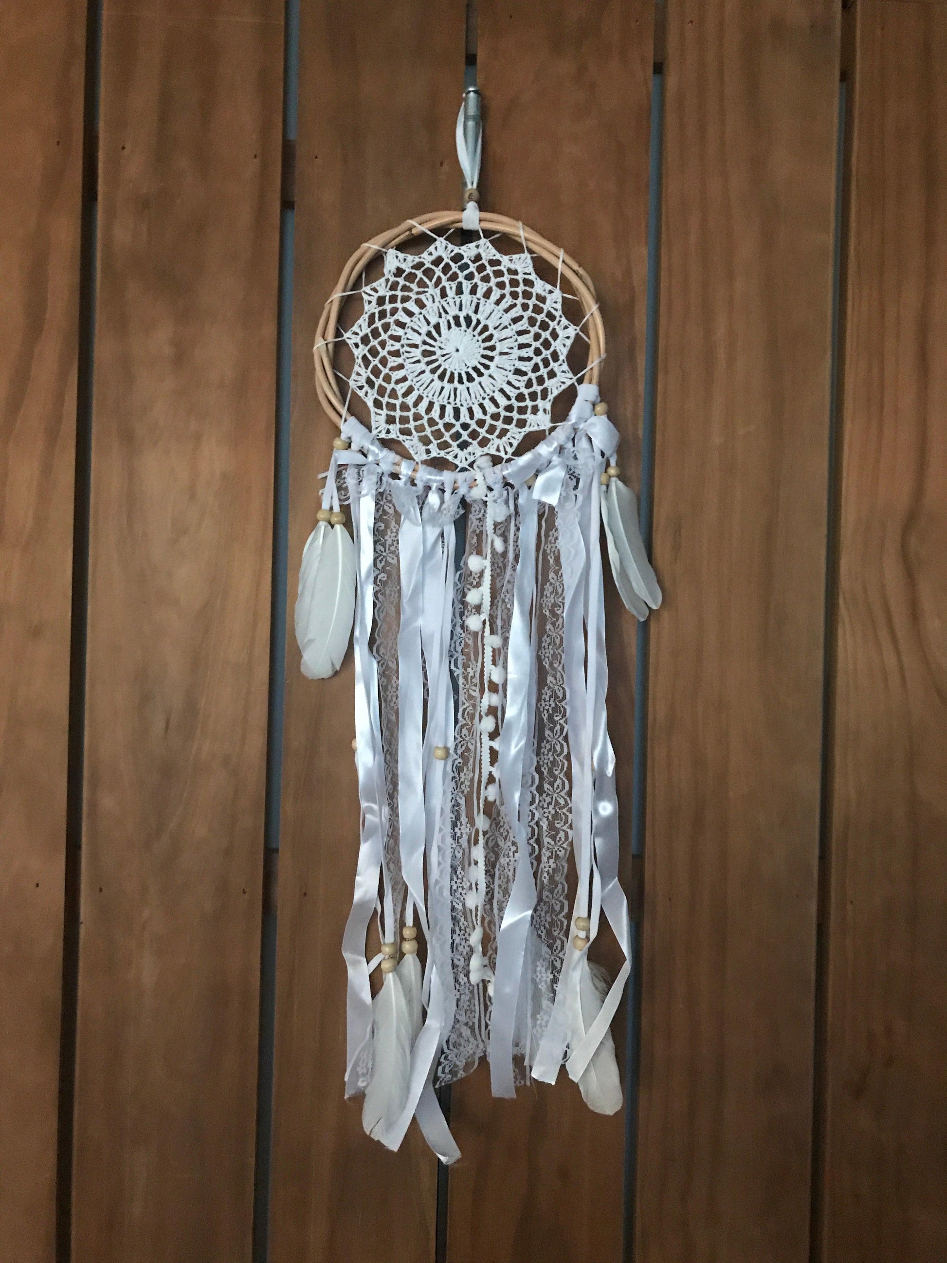 Handmade 22cm white dream catcher with intricate web, hanging feathers, and ribbons on wooden background.