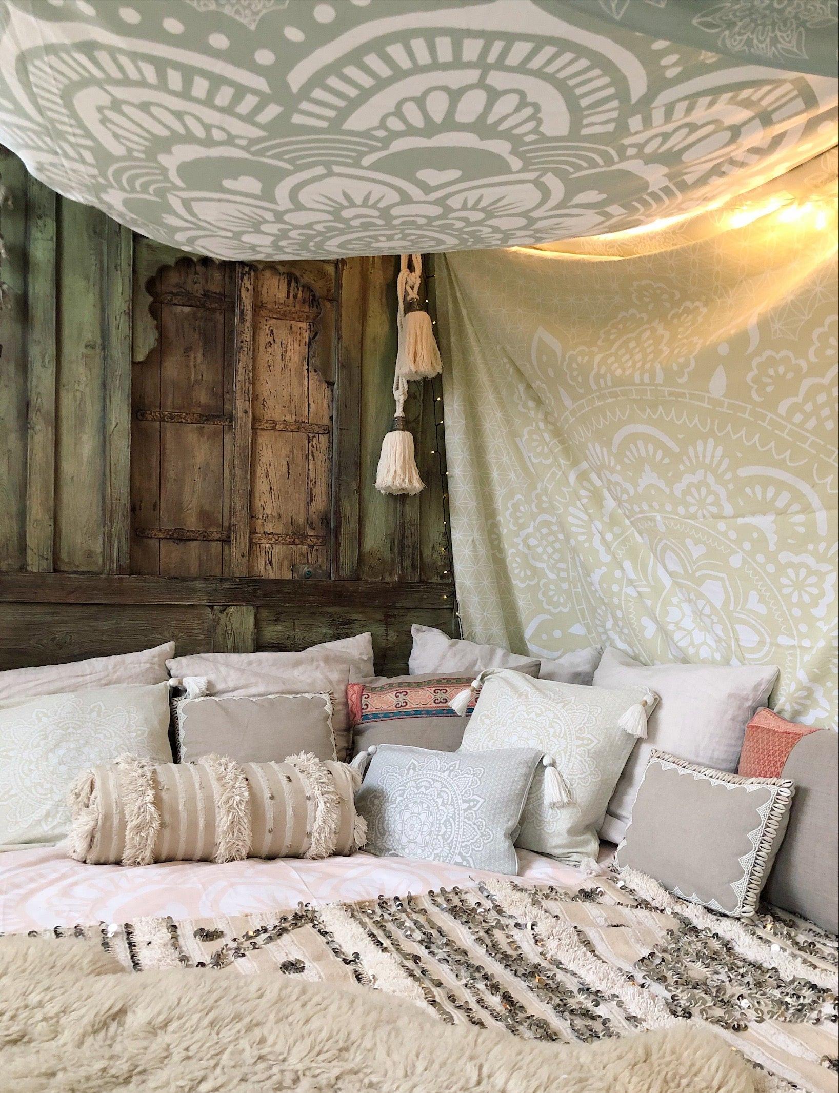 Khaki tapestry with intricate white mandala design hanging above a bed with neutral pillows and textured cushions.