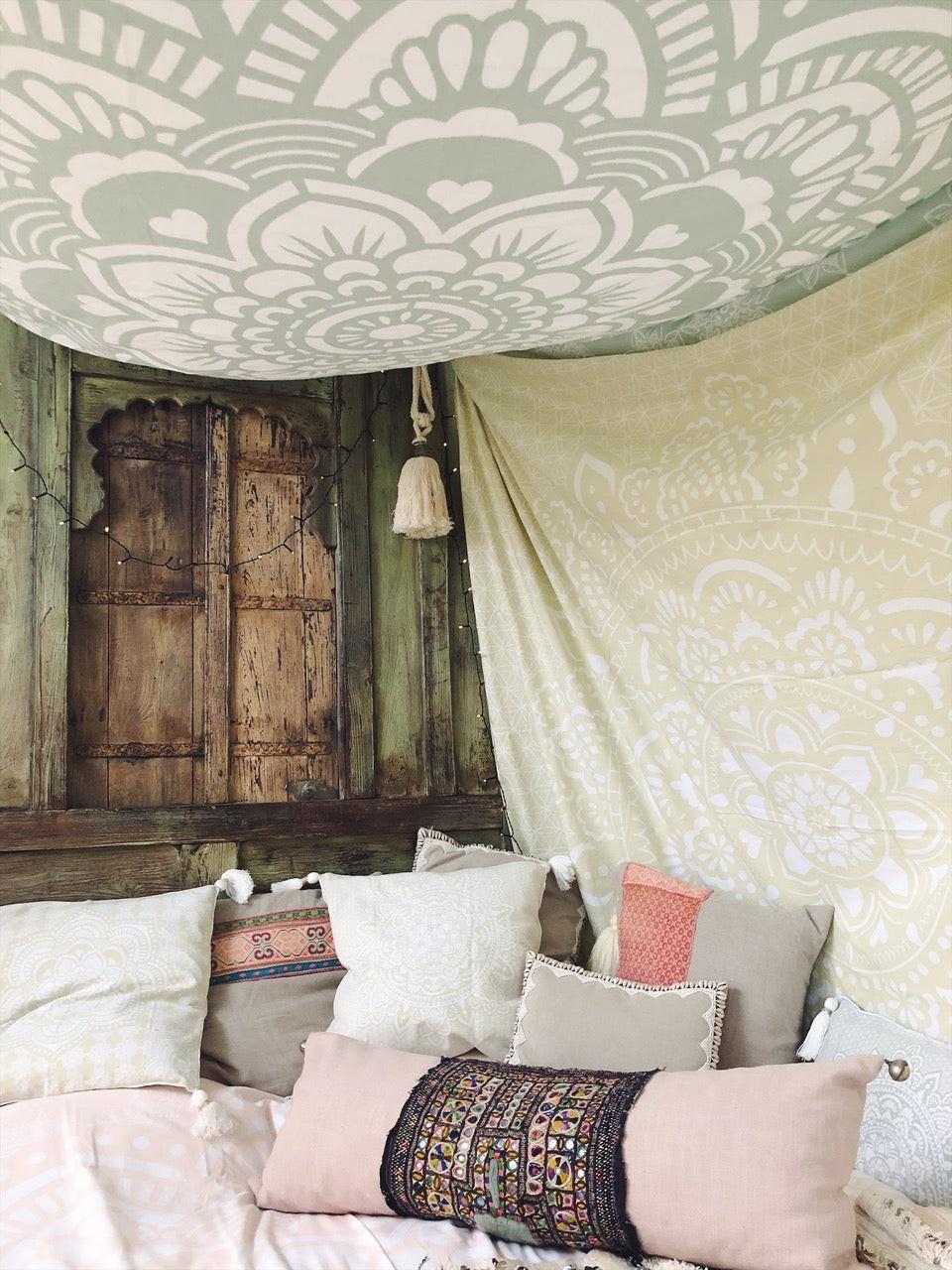 Khaki tapestry with intricate holy mandala design hanging on wall above rustic wooden doors and sofa with cushions.