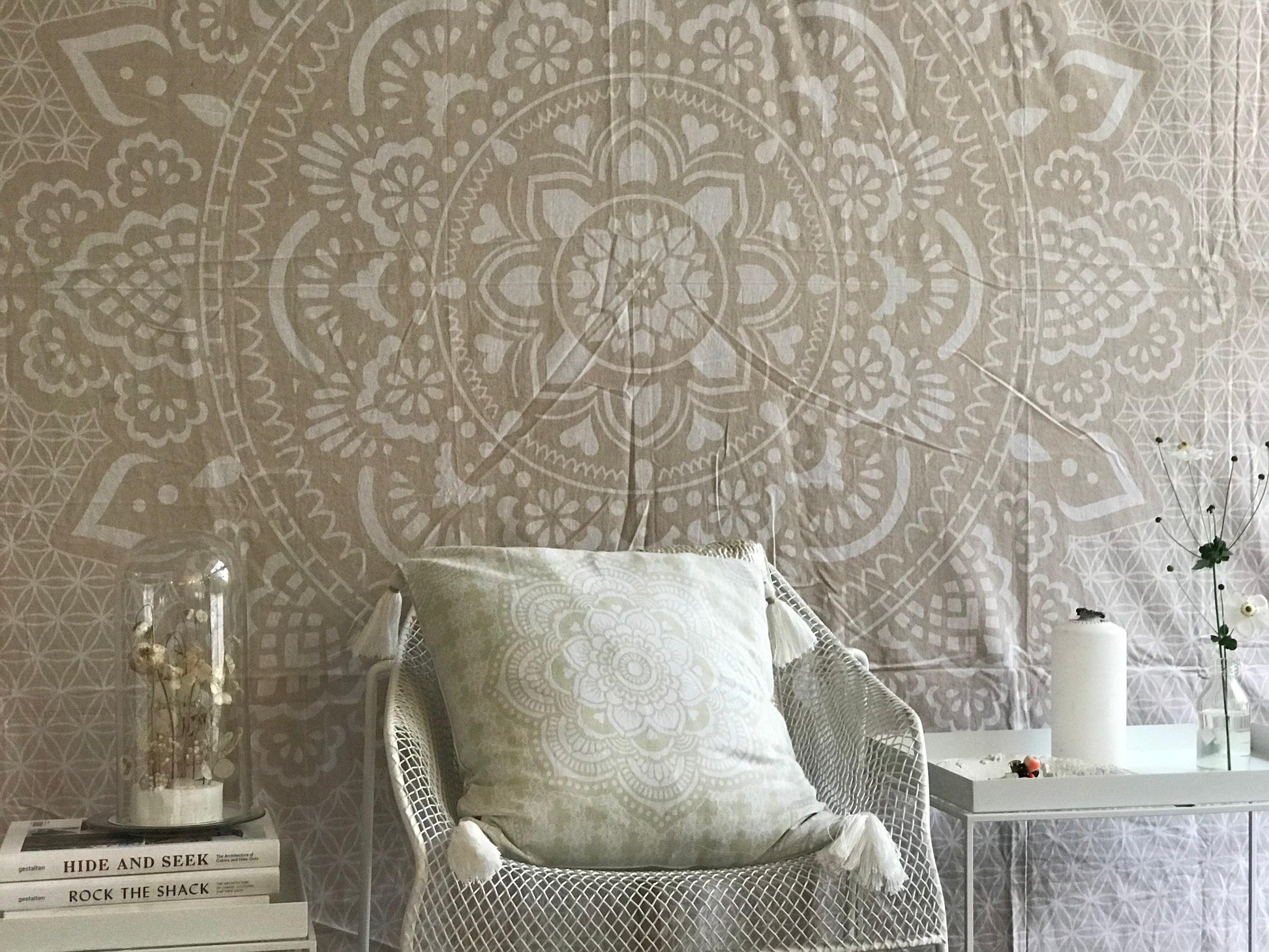 Khaki tapestry with intricate holy mandala design in beige and white tones displayed behind a chair with a matching cushion.