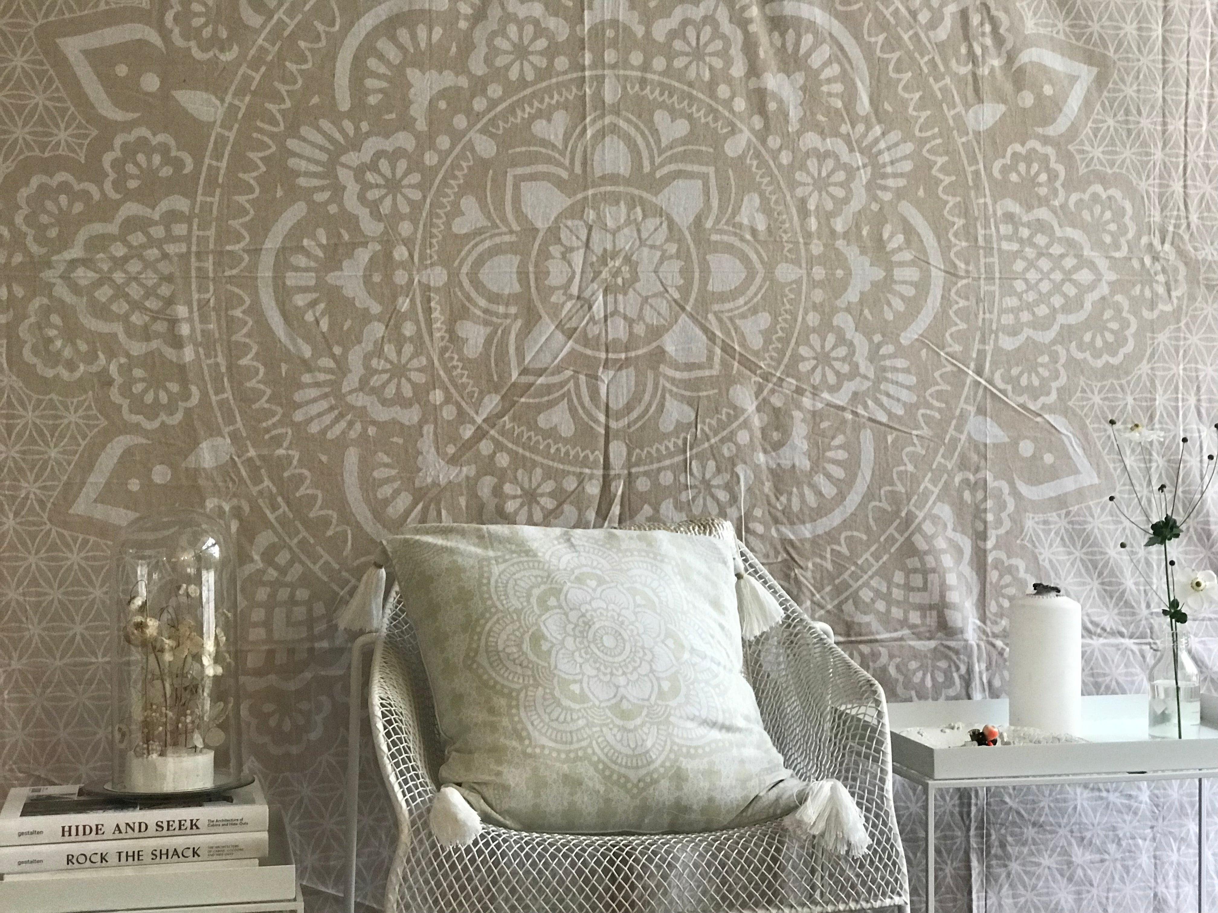 Khaki tapestry with intricate holy mandala design in beige and white tones displayed behind a chair with a matching cushion.