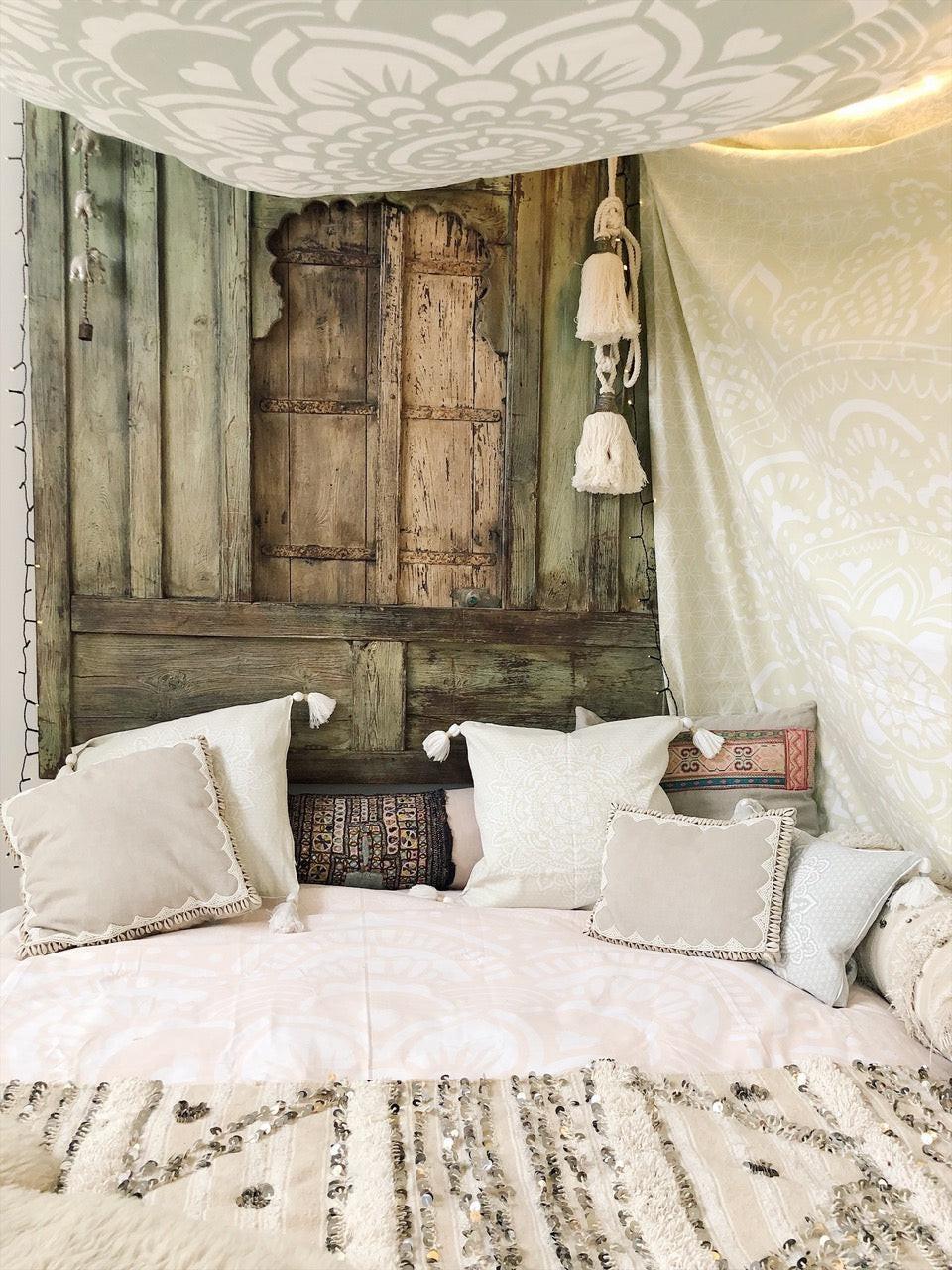 Khaki tapestry with intricate holy mandala pattern hanging over rustic wooden wall above beige cushions and textured rug.