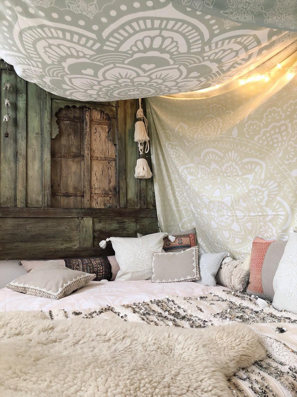 Khaki tapestry with white intricate mandala pattern hanging above and on wall in cozy bedroom setting with pillows and.