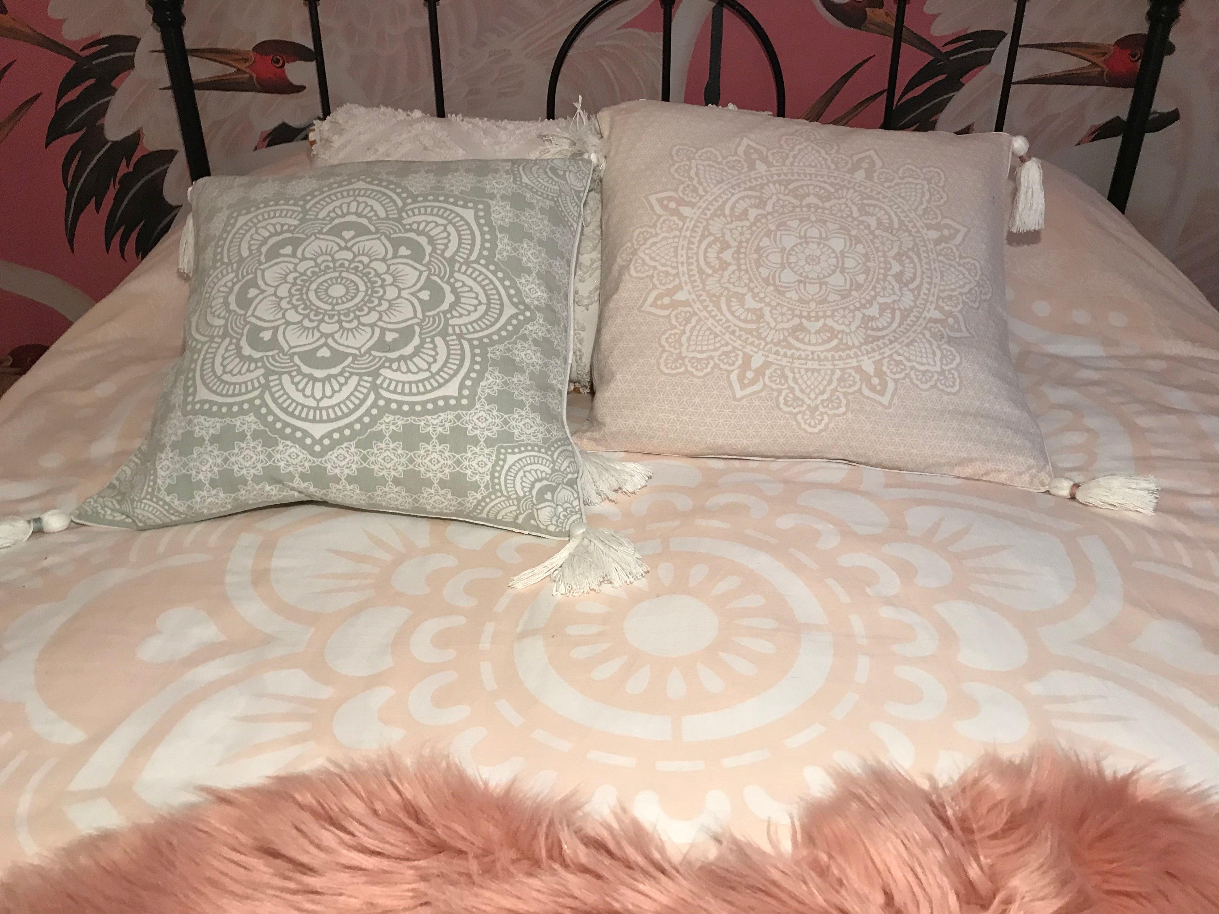 Square cushion with intricate white mandala print on soft pink fabric, 50x50 cm, tassels on corners.