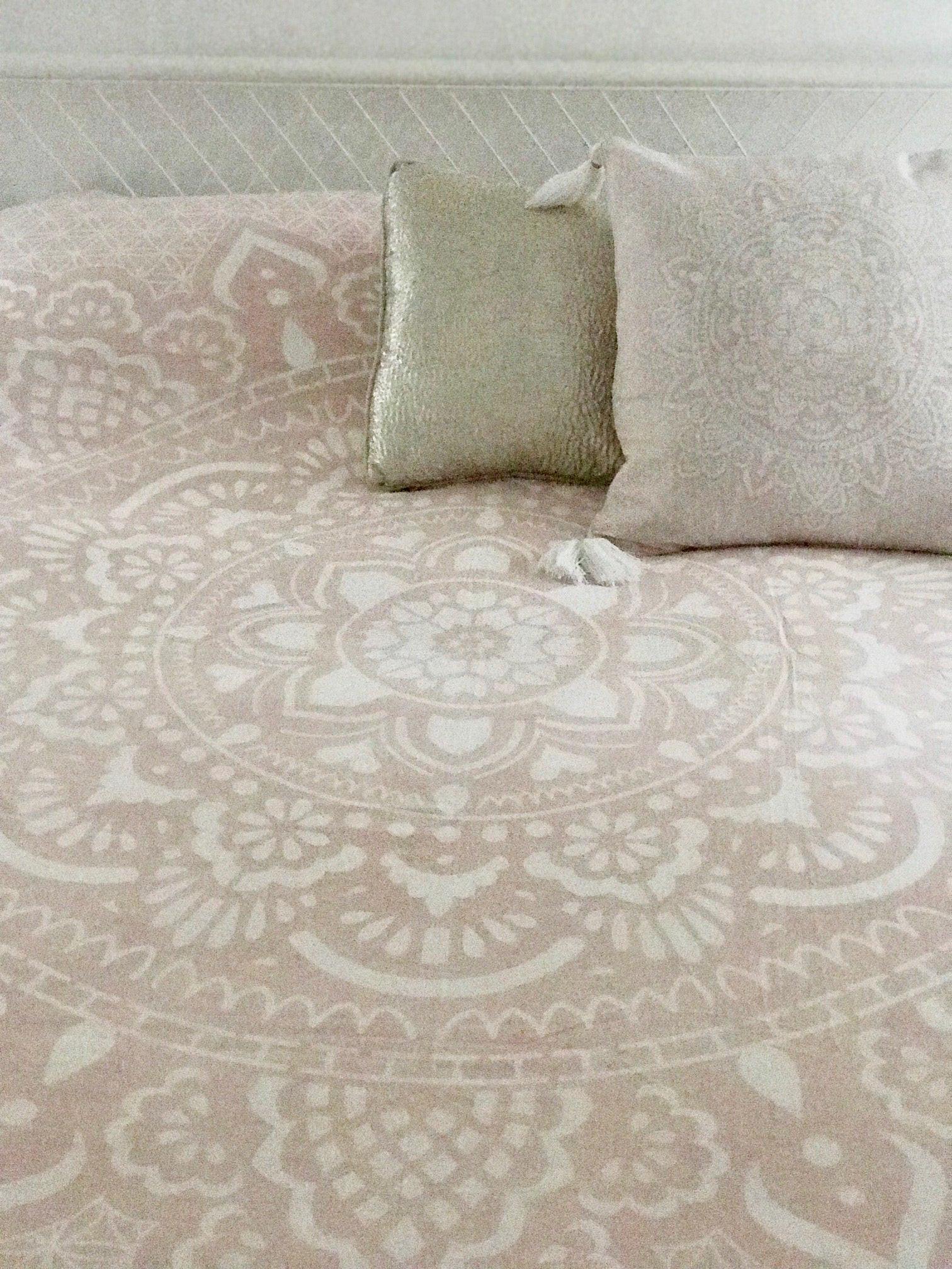 Pink bed cover with intricate mandala pattern, paired with textured beige throw pillows.