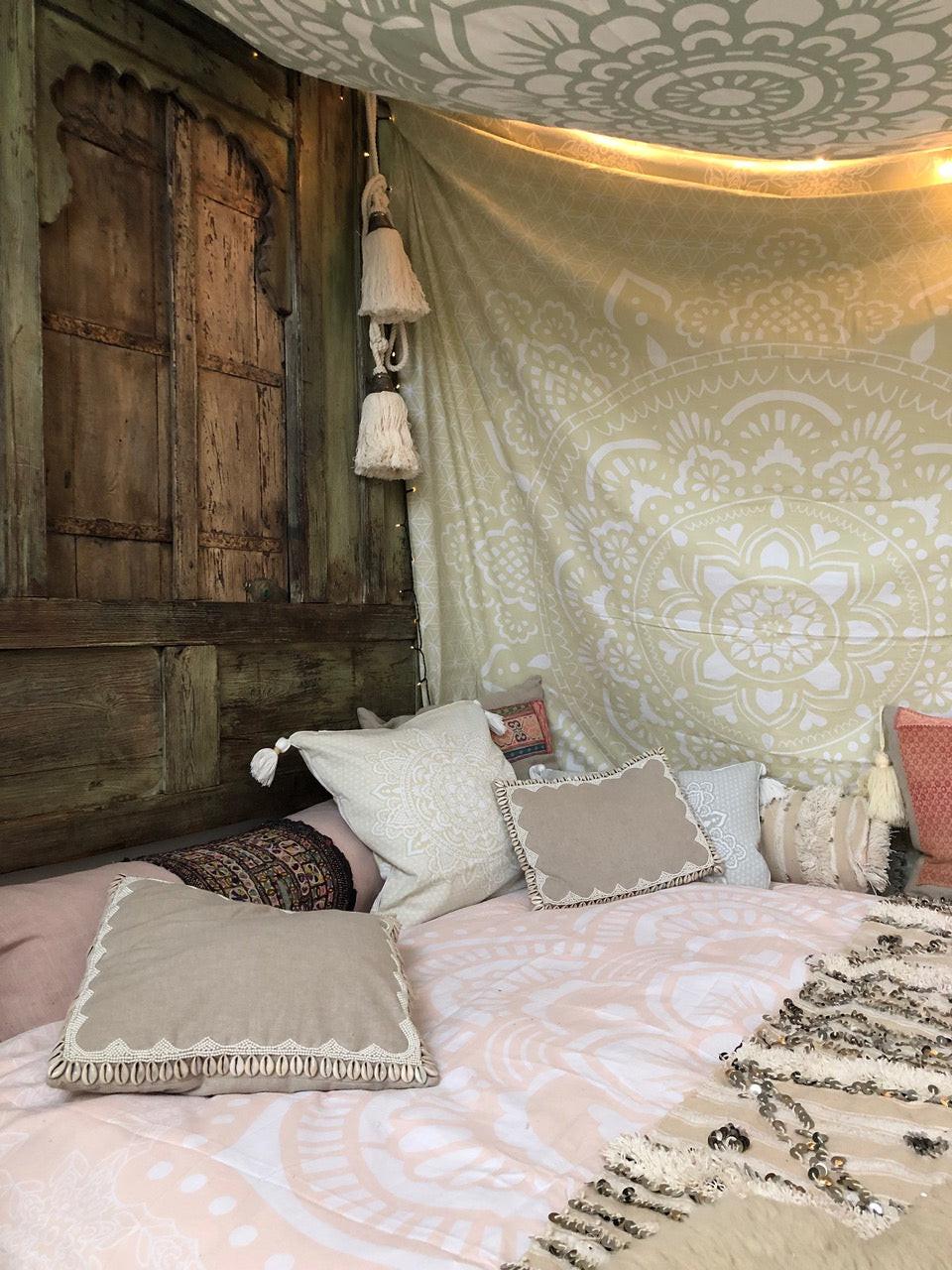 Khaki tapestry with intricate holy mandala pattern hanging on rustic wooden wall above bed with neutral-toned pillows and.