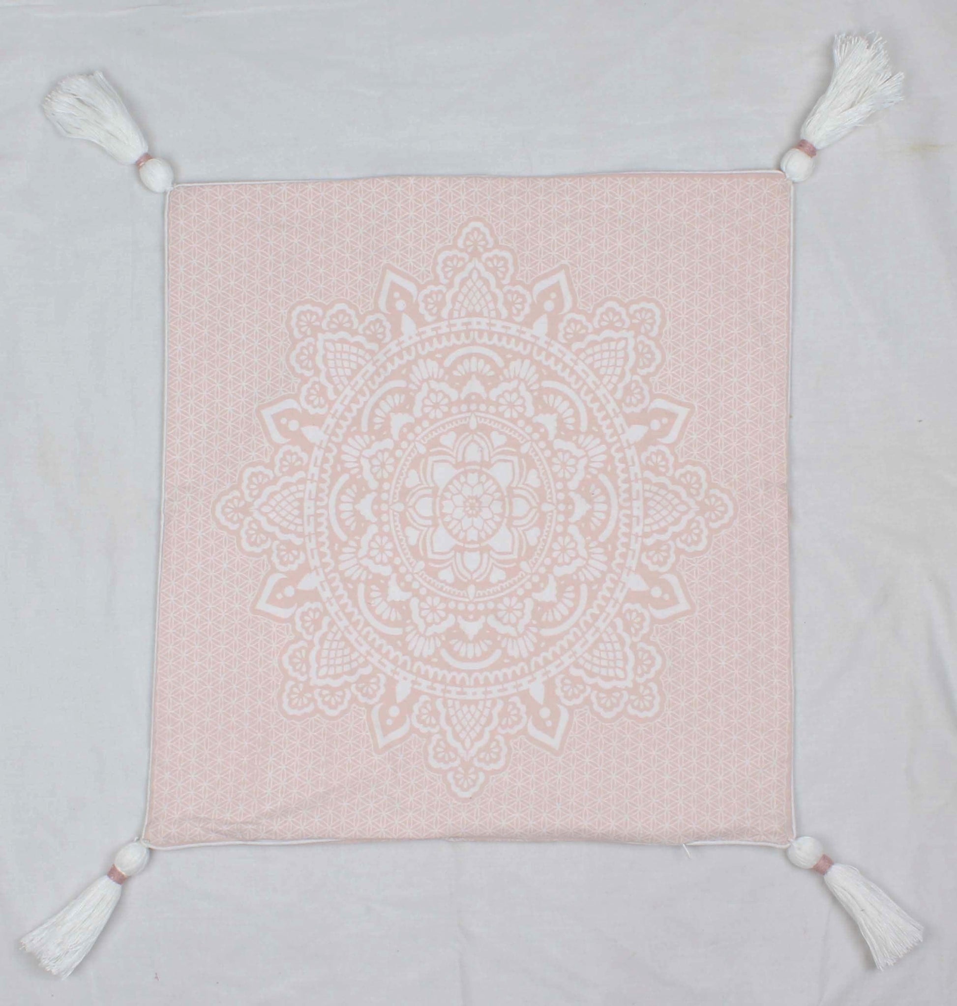 Square pink cushion cover with white intricate mandala print and tassels on each corner.