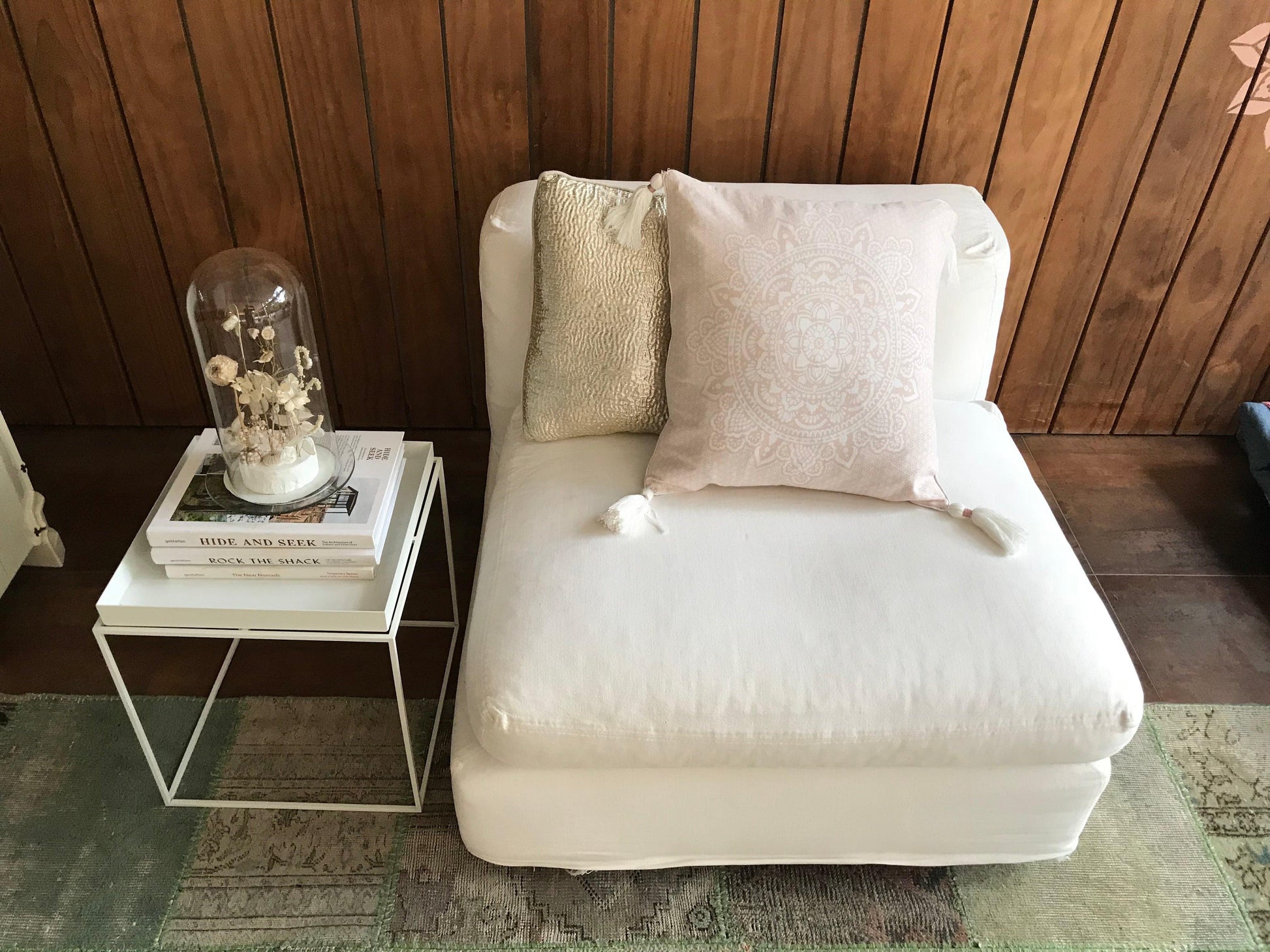 Pink cushion with intricate white mandala design and tassels on cream armless lounge chair.