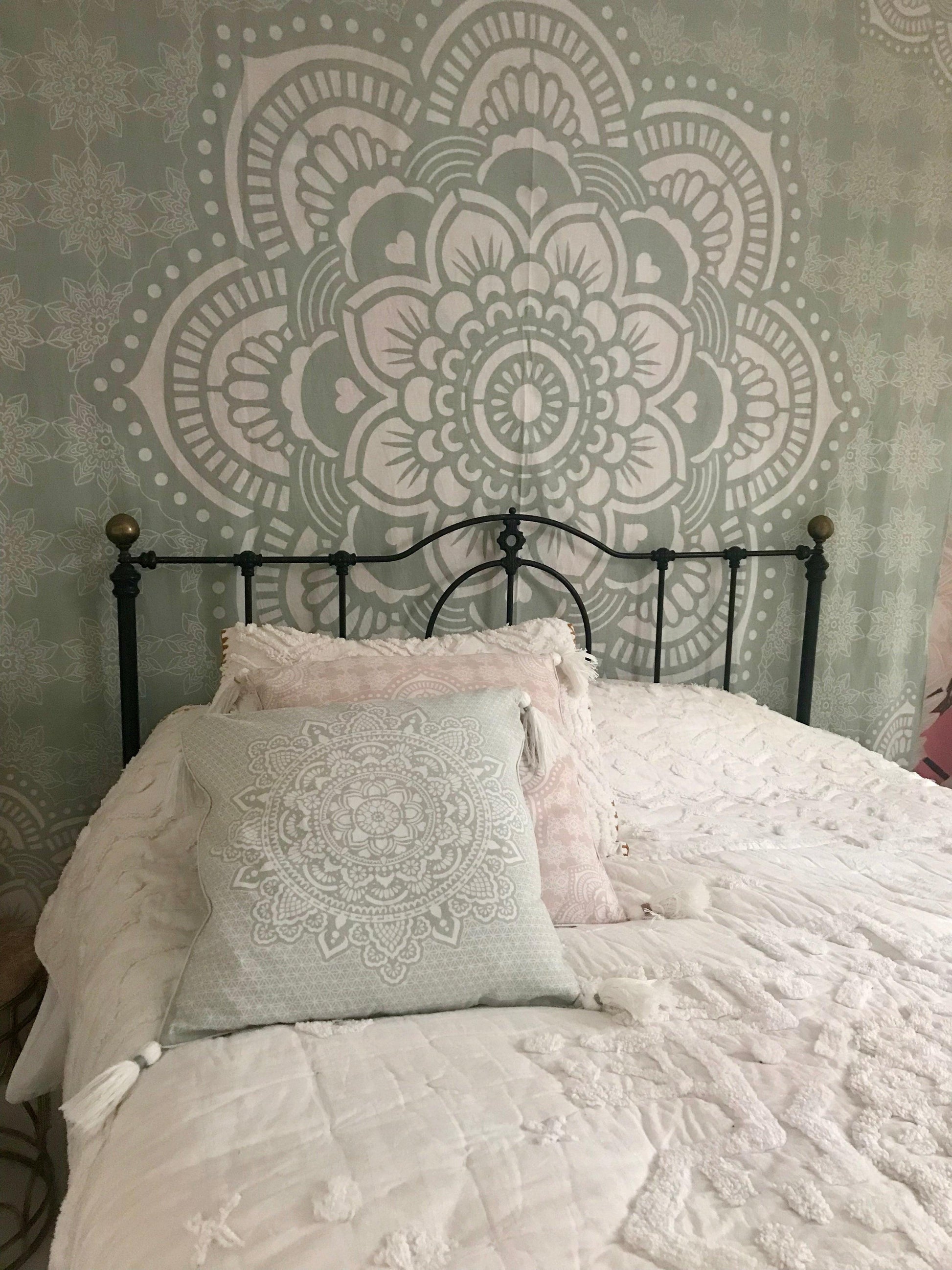 Mint green cushion with intricate white mandala design on a black metal bed frame with white bedding.