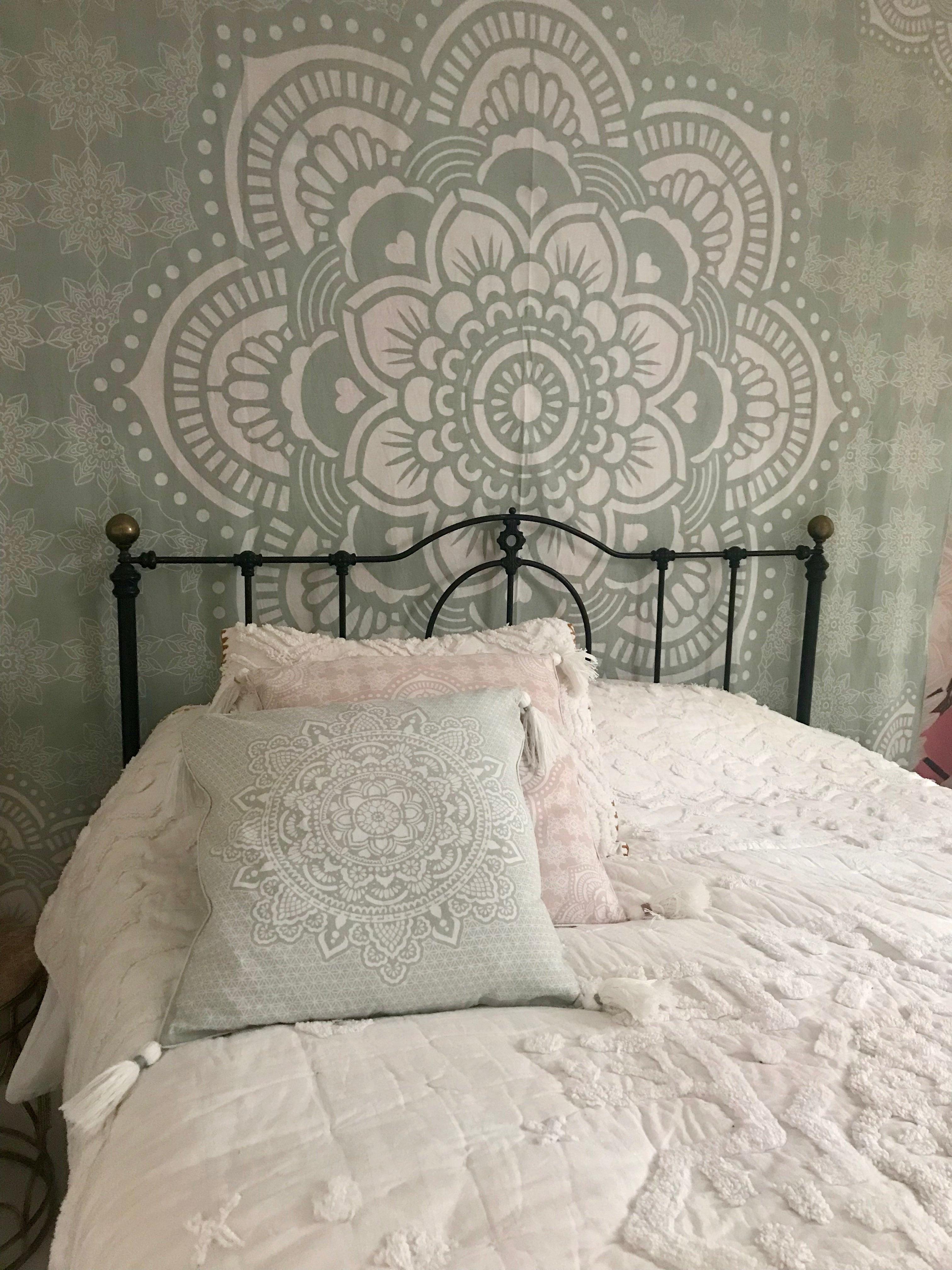 Mint green cushion with intricate white mandala design on a black metal bed frame with white bedding.
