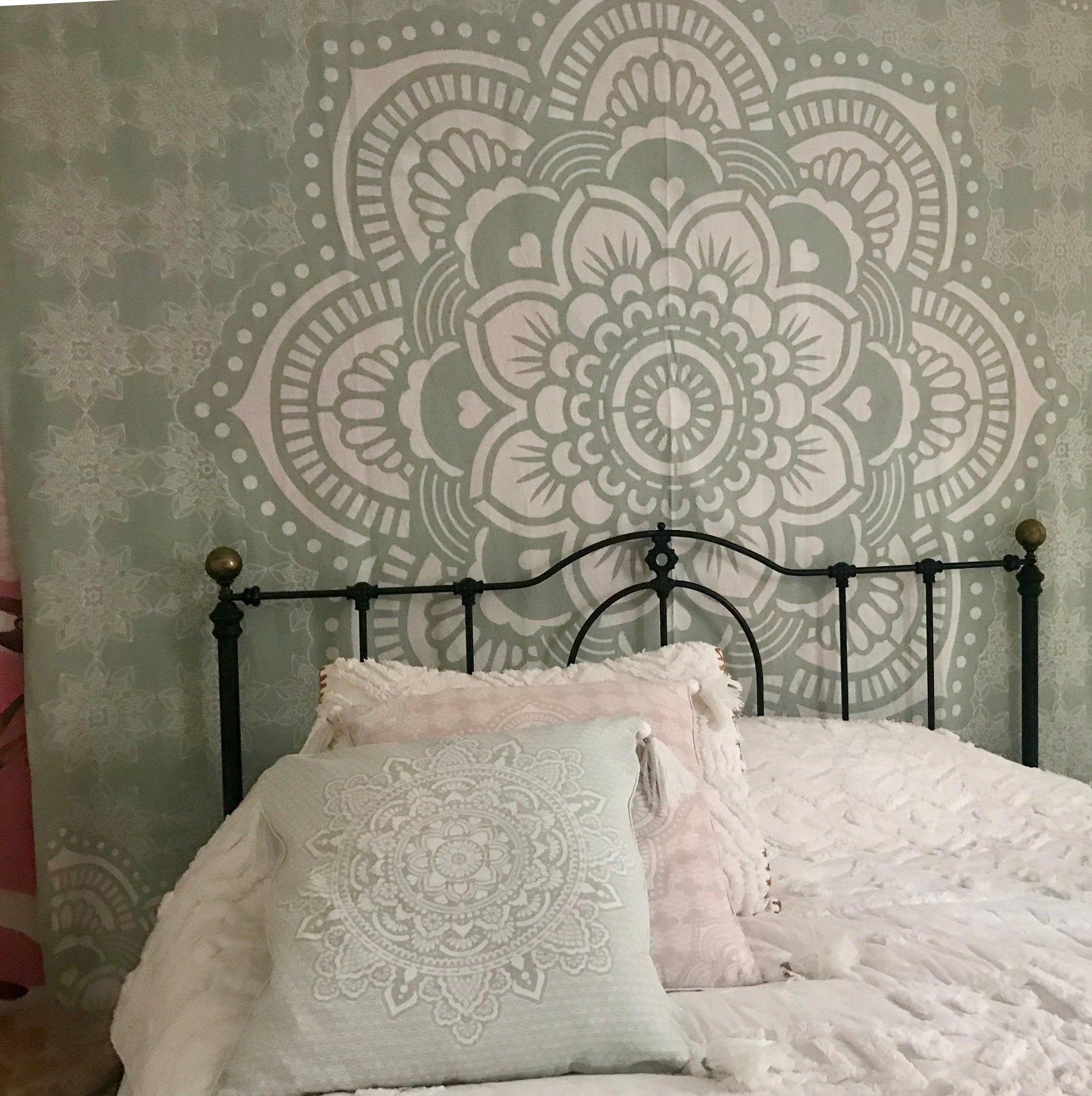 Mint green cushion with intricate mandala embroidery on a black metal bed frame.