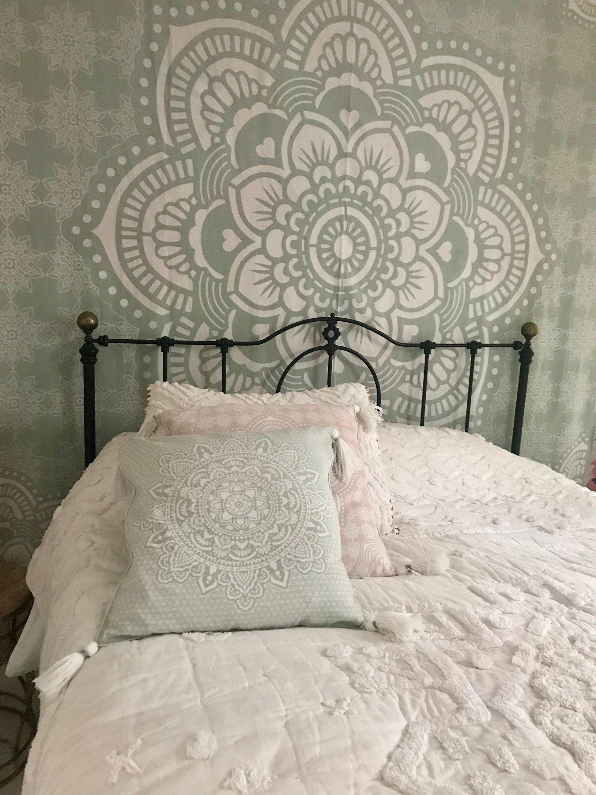 Mint green cushion with intricate white mandala embroidery on a black metal bed frame.
