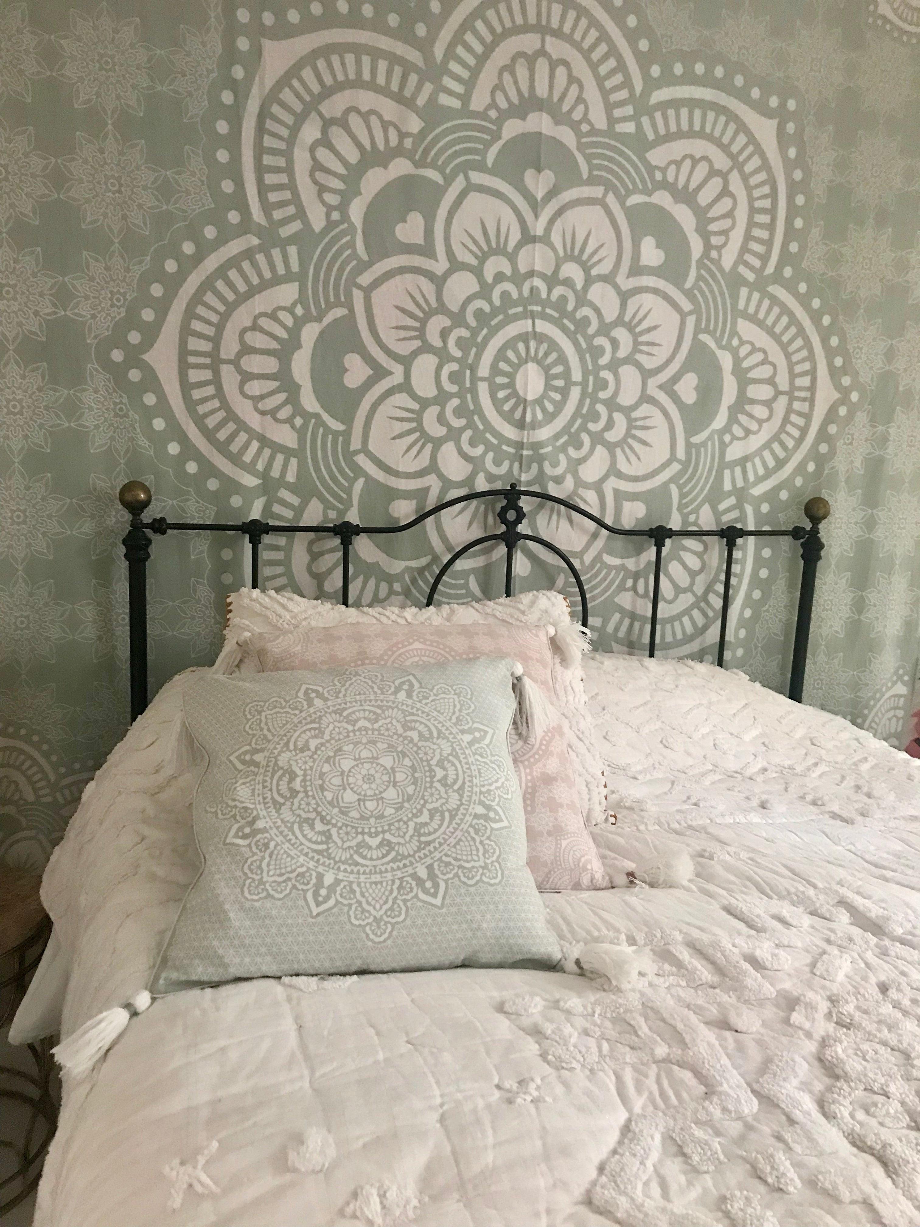 Mint green cushion with intricate white mandala embroidery on a black metal bed frame.