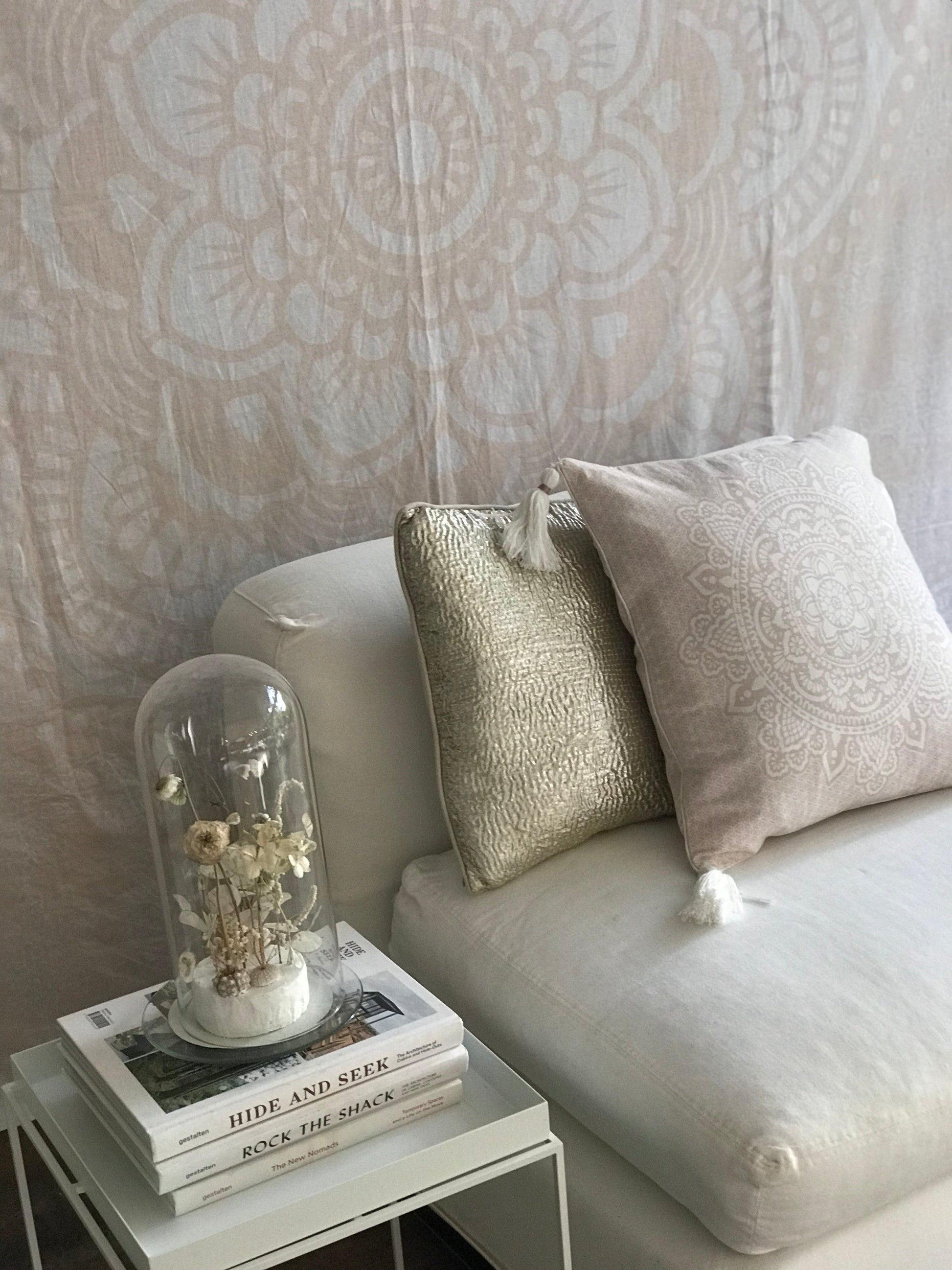 Pink square cushion with intricate mandala pattern on white couch next to beige textured pillow.