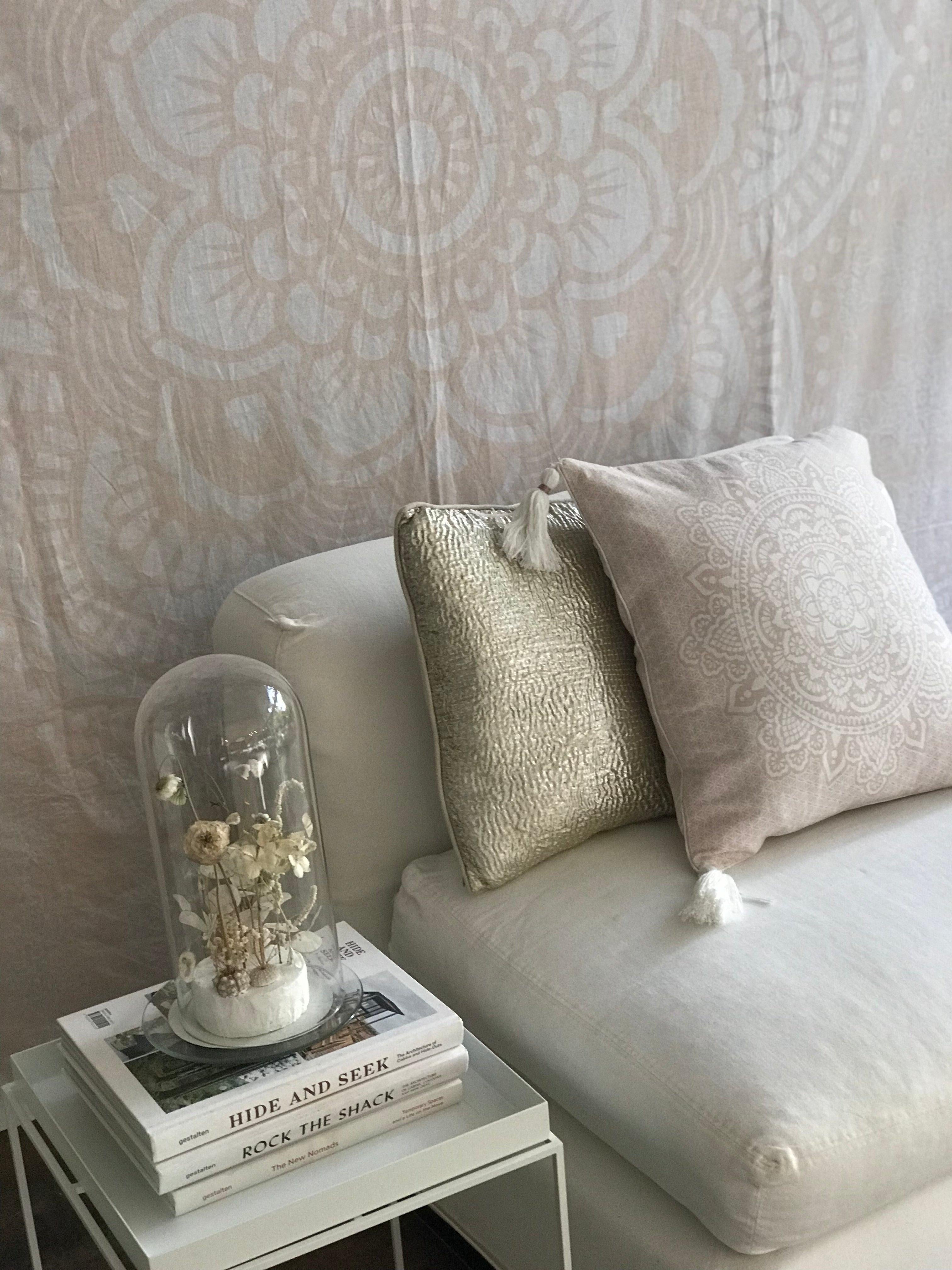 Pink square cushion with intricate mandala pattern on white couch next to beige textured pillow.