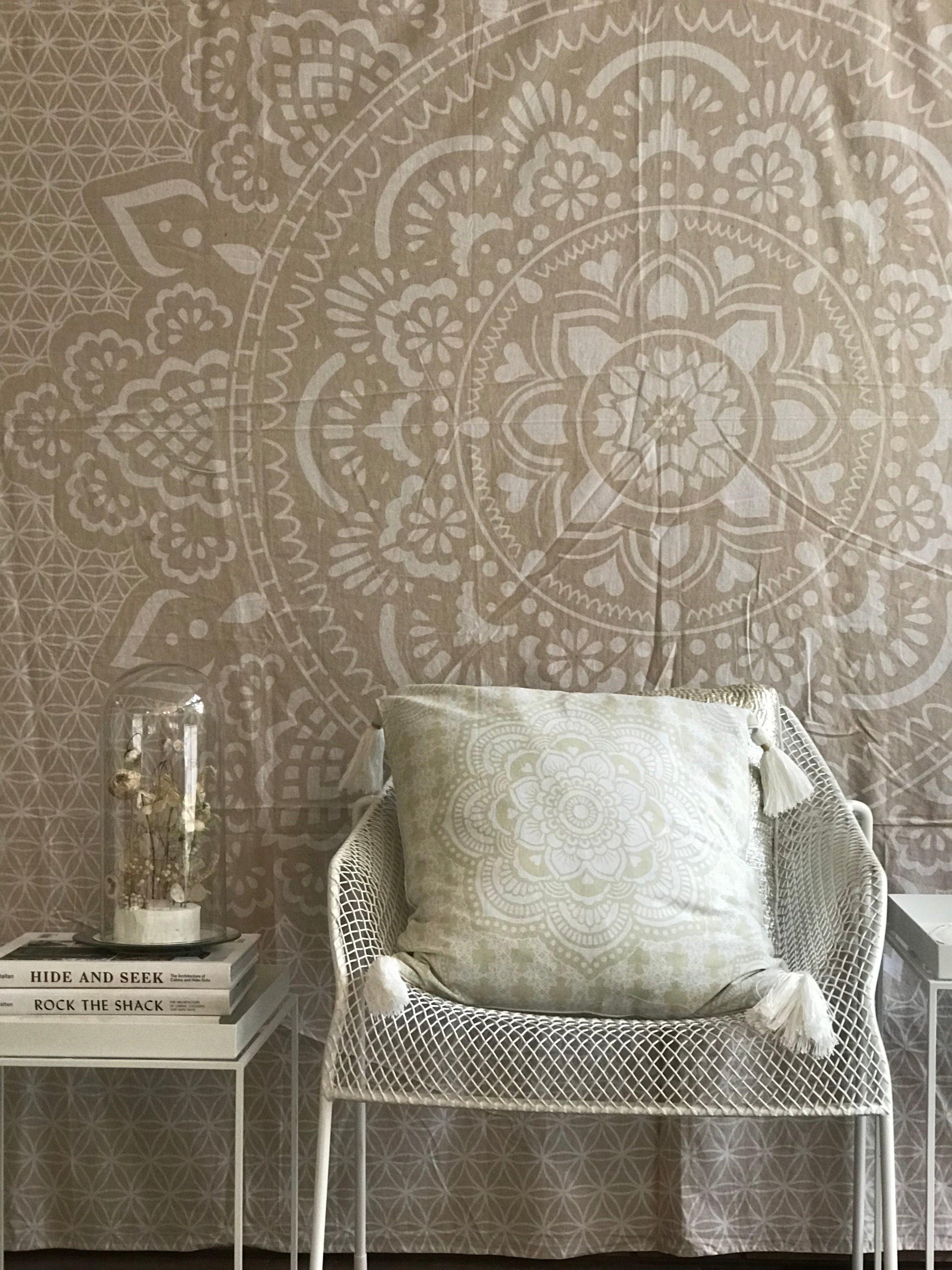 Khaki tapestry with intricate white holy mandala pattern behind white mesh chair with pale green cushion and stack of books.