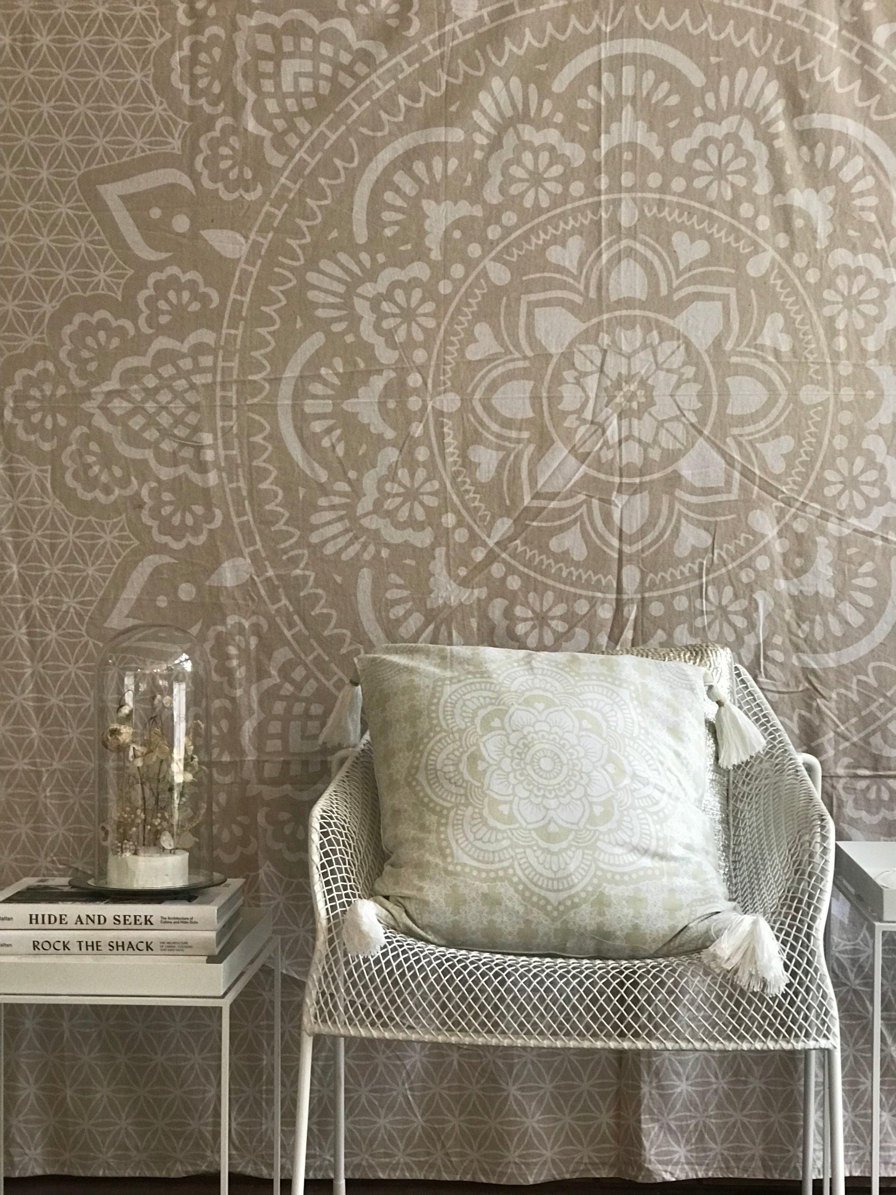 Khaki tapestry with intricate white holy mandala pattern behind white mesh chair with pale green cushion and stack of books.
