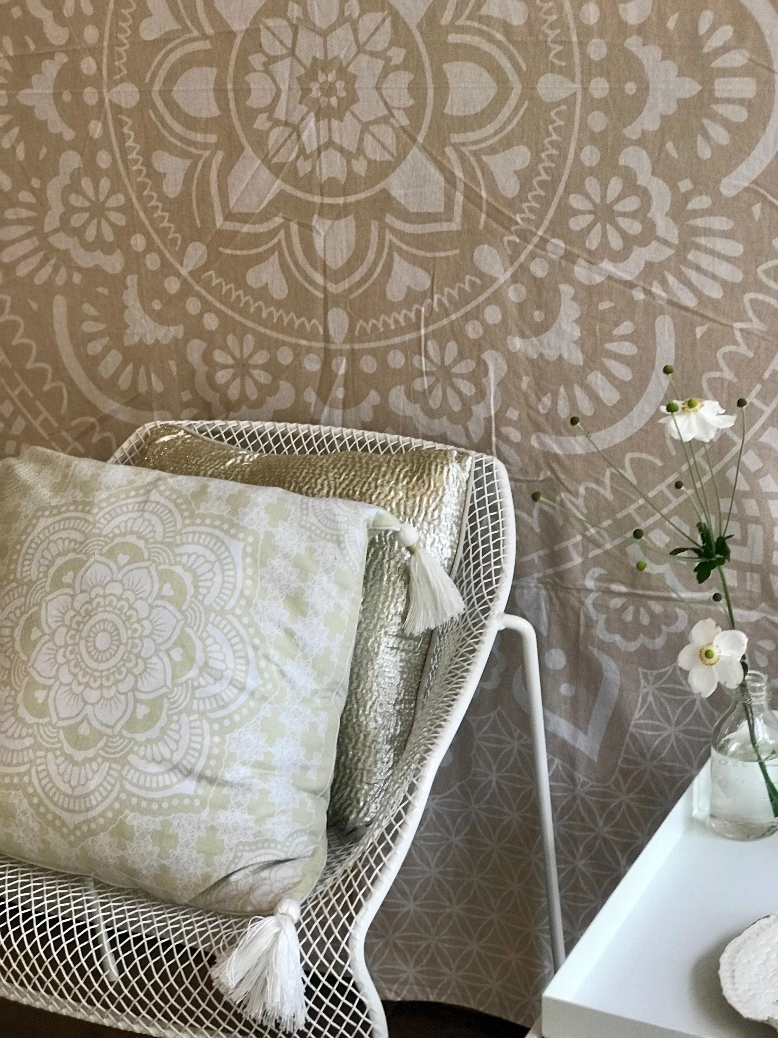 Khaki tapestry with intricate white holy mandala design hung behind white mesh chair with matching cushion and nearby white.