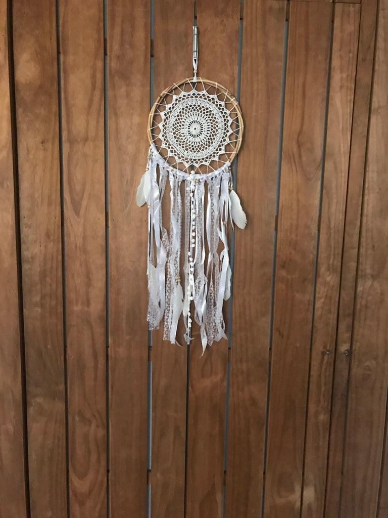 Handmade beige dream catcher with intricate web and white feathers hanging on wooden wall.