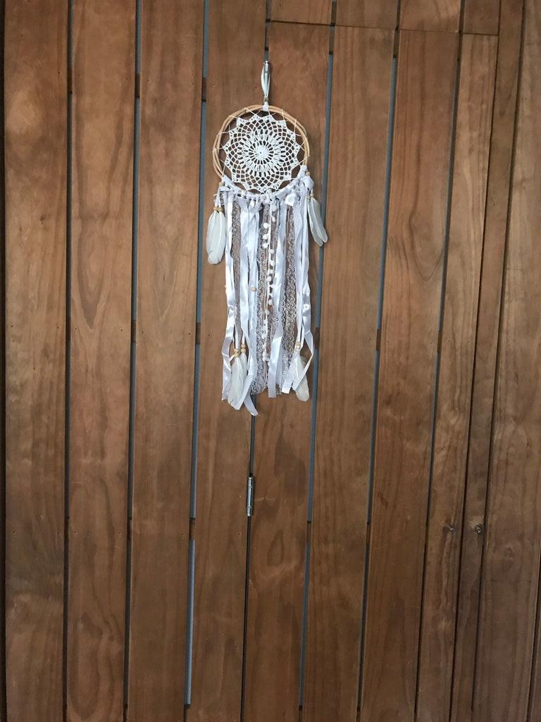 Small handmade white dream catcher with intricate web and hanging feathers on wood background.