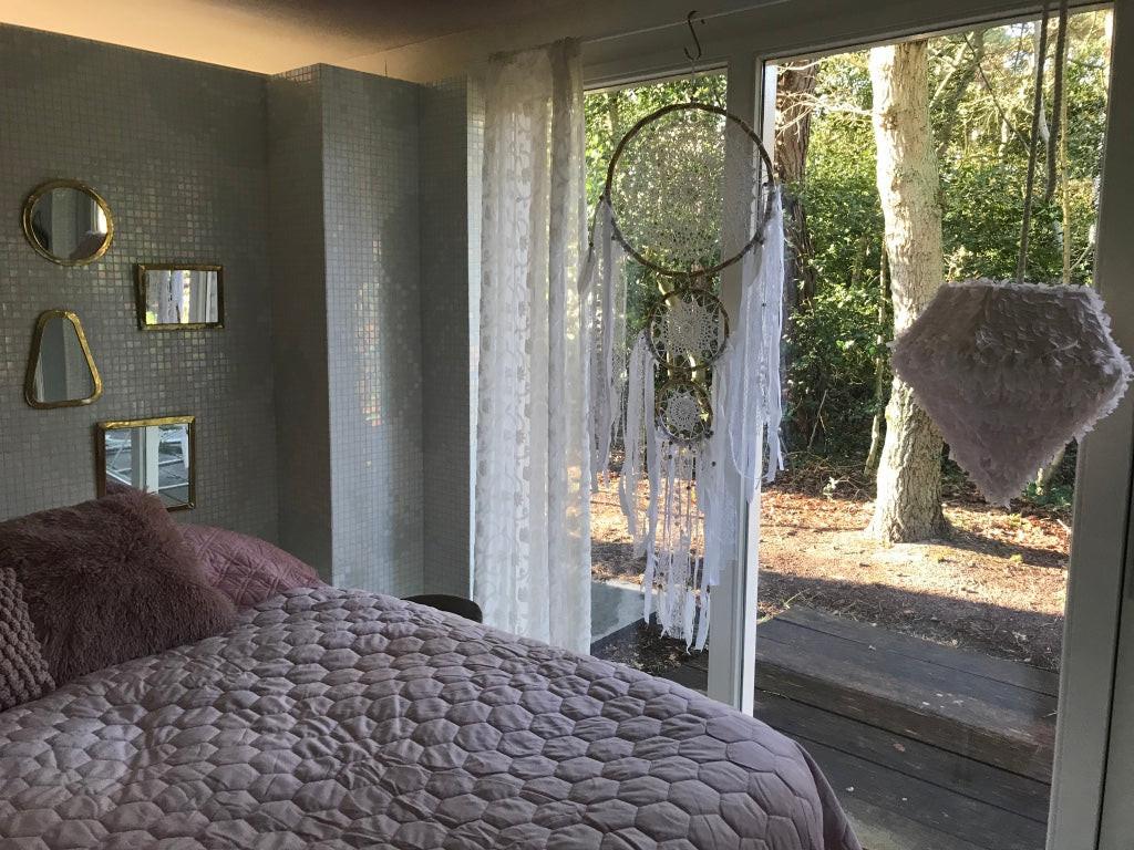 Boho dreamcatcher trio with white feathers and lace hanging in soft bedroom light by window.
