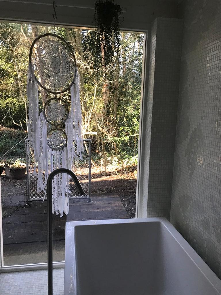 Triple hoop dream catcher with white feathers and fringe hanging by glass door in natural light.